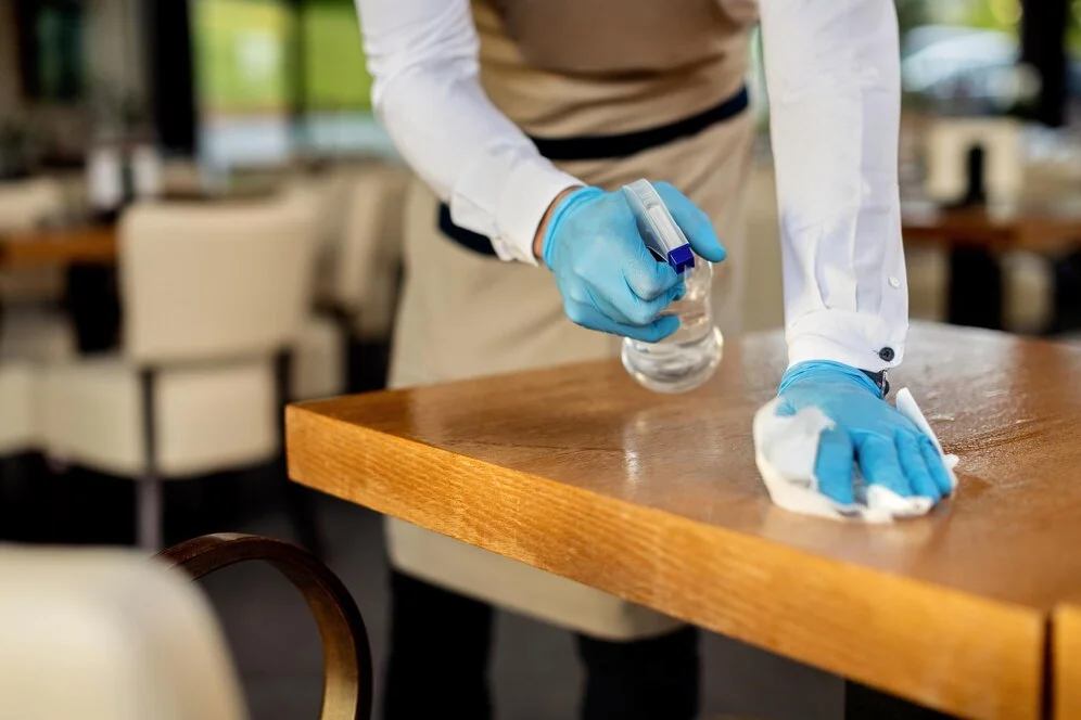A person from a San Francisco maid service sanitizing a table with a cloth.