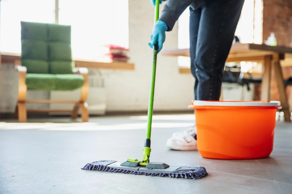 Person mopping the floor near an orange bucket with San Francisco maid service assistance.