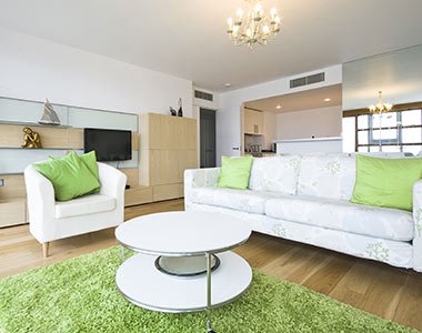 Modern living room with white furniture, green accents, and maintained by a house cleaning company.